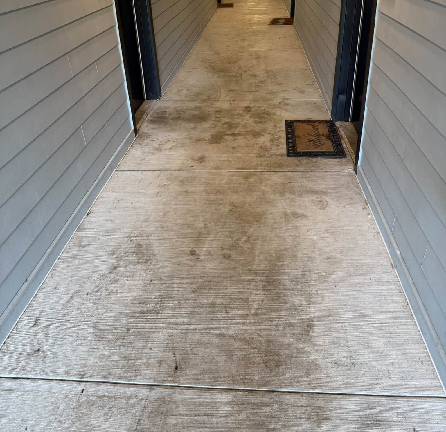 A covered apartment breezeway floor tracked with dirt before commercial pressure washing