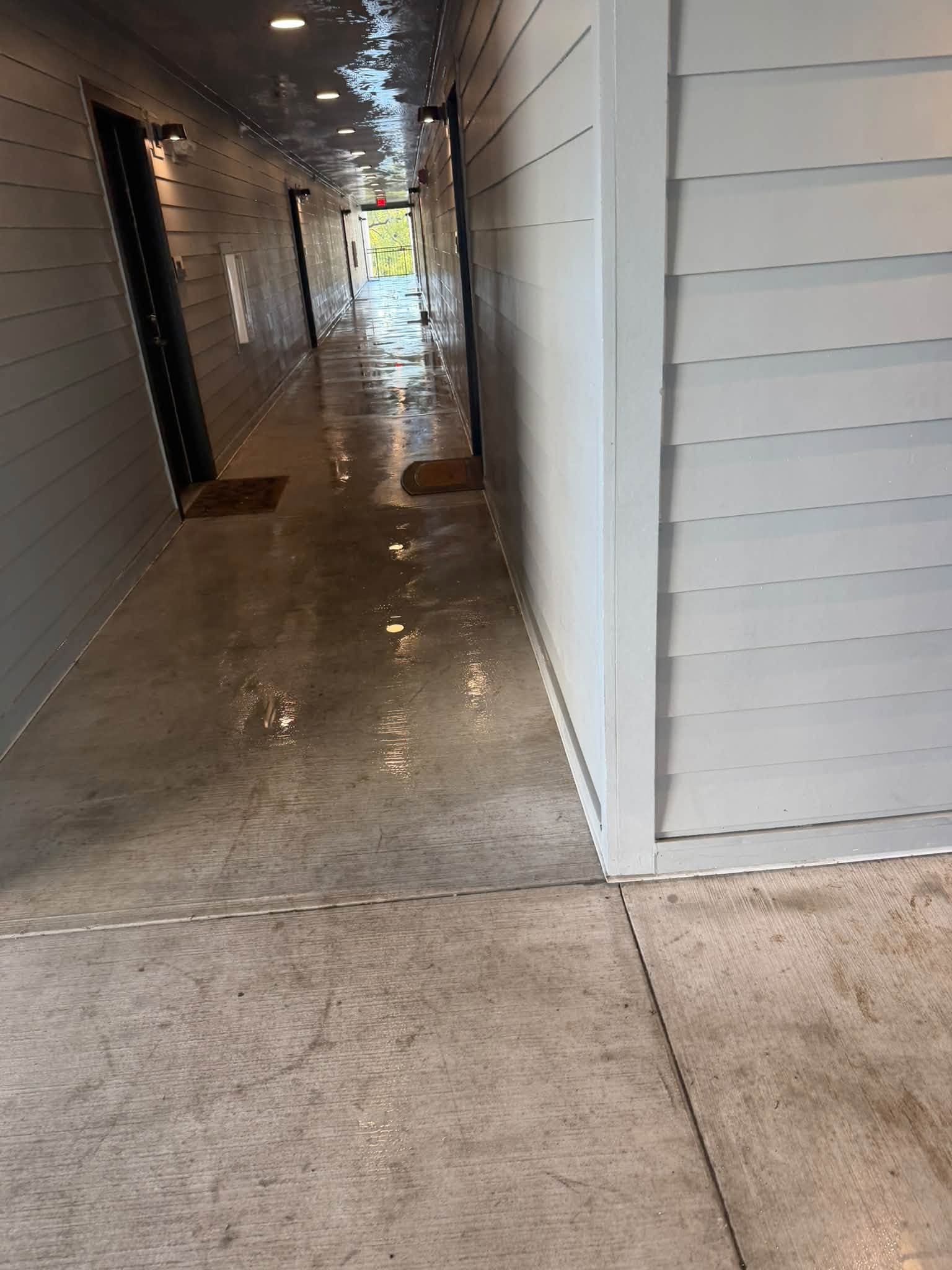 An apartment breezeway partway through commercial pressure washing, wet clean floor ahead