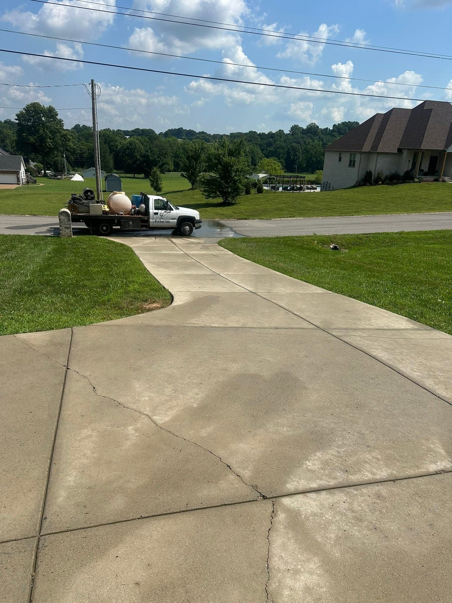 A driveway partway through concrete cleaning, clean lanes beside darker slab