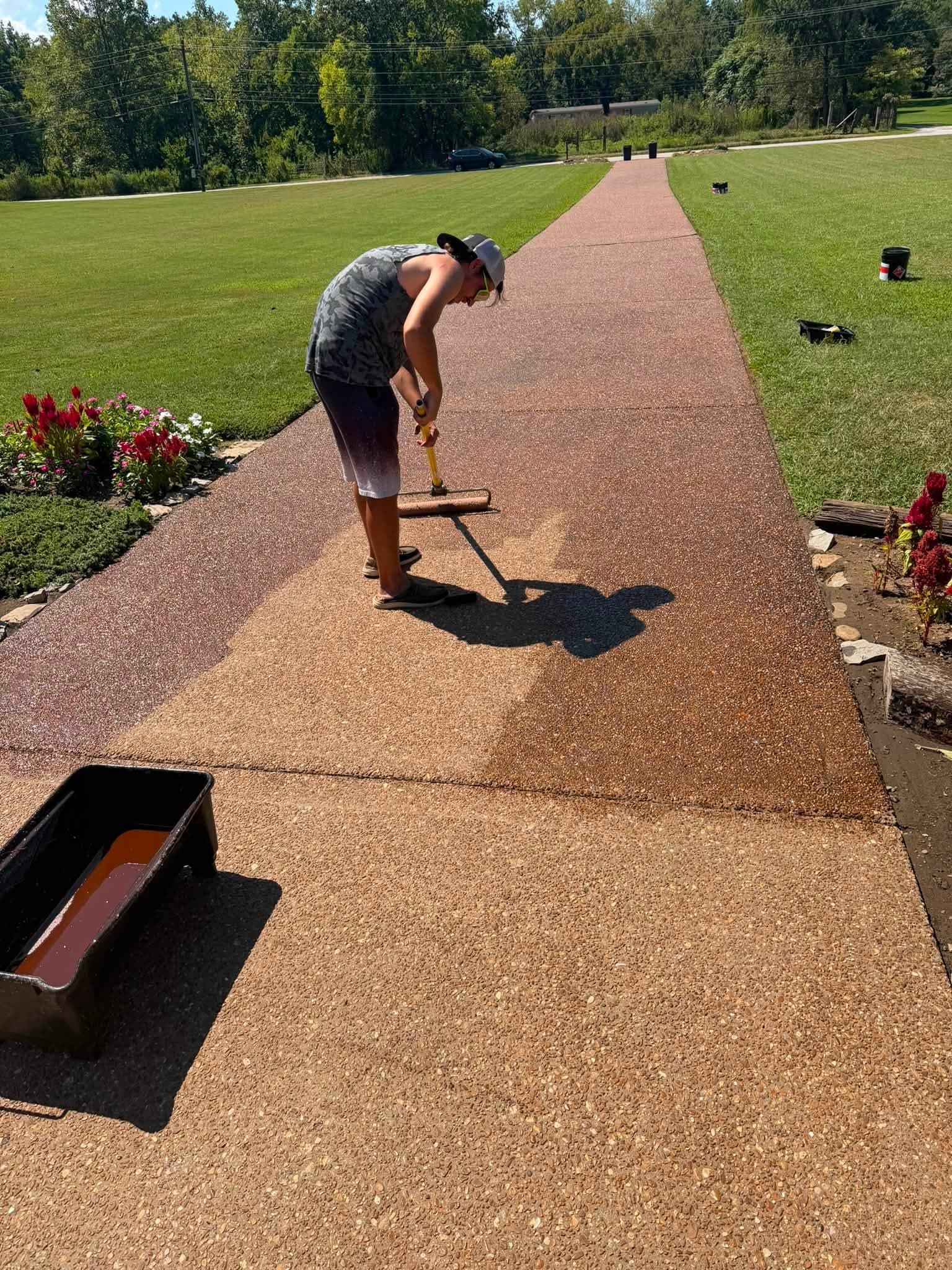 A crew member rolling sealer onto an exposed-aggregate walk during driveway sealing