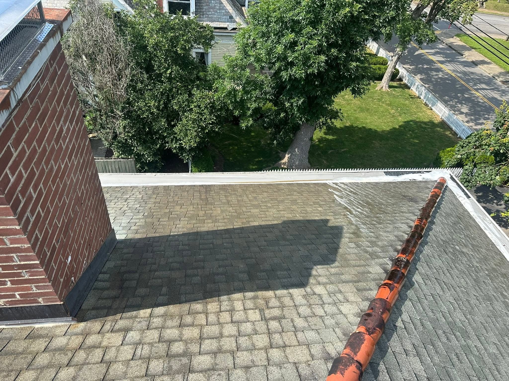 Shingles beside a brick chimney, darkened with growth, partway through a roof wash